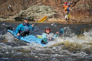 Two people in a tandem kayak as waves from river rapids splash around them