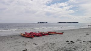 Sea kayaks on a sandy beach getting ready to launch, with and island and headland in the background 