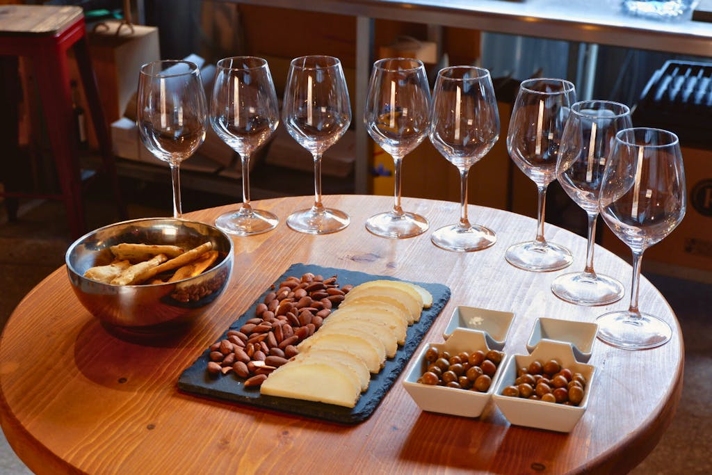 a wooden table topped with glasses of wine and cheese, nuts and meats