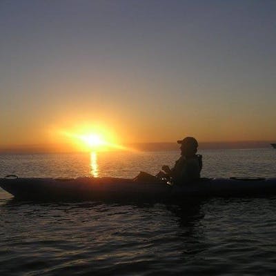 a man sitting in a boat on a body of water in the sunset