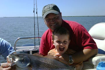 a man and a child holding a caught fish on a boat in a body of water