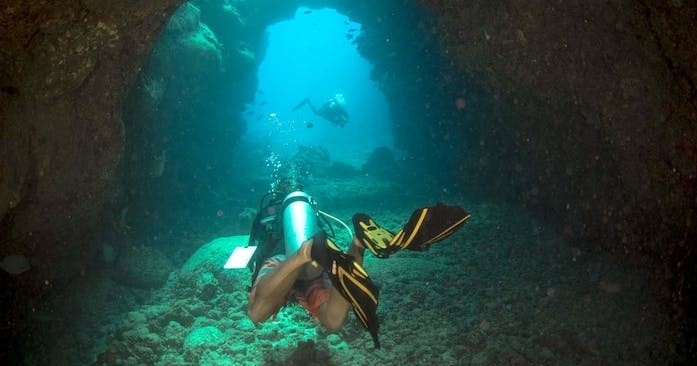 A scuba diver is exploring an underwater cave during an adventurous dive in Kauai, with Fathom Five Divers.