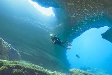 A diver is swimming through a rocky underwater cave during a dive in Tunnels, Kauai, with Fathom Five Divers