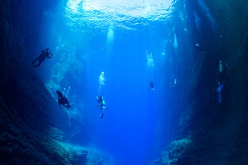 Scuba divers suspended in the deep azure waters during a tour, bubbles rising towards the ocean surface. niihau