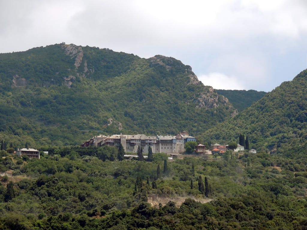 Exterior view of Xiropotamou Monastery, surrounded by lush greenery, with Mount Athos in the background.