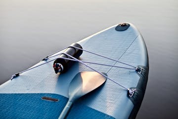 Paddleboard and surf board with paddle on blue water surface background close up. Surfing and SUP boarding equipment in sunset lights close-up. Outdoor water sports. Surfing lifestyle backgrounds.