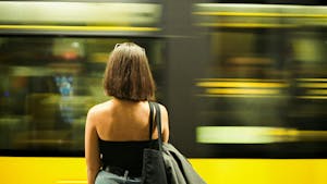 A woman standing on the platform gazes at a Metro train passing by in Porto, Portugal
