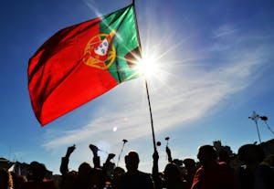 Portuguese flag waving with people holding up carnations in celebration of the Carnation Revolution