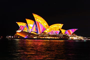 a boat that is lit up at night with Sydney Opera House in the background