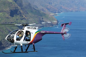 a doors-off helicopter flying over a body of water with mountains in the background