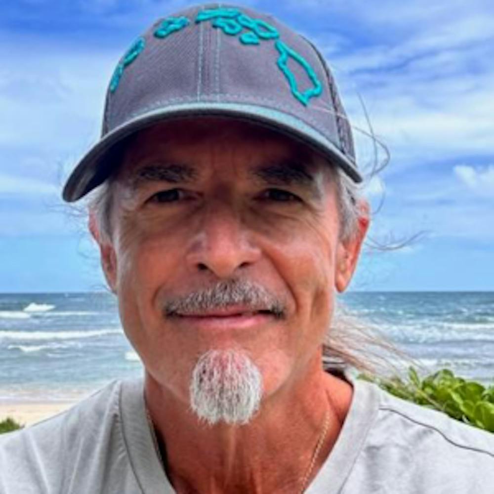 a man wearing a hat and smiling at the ocean