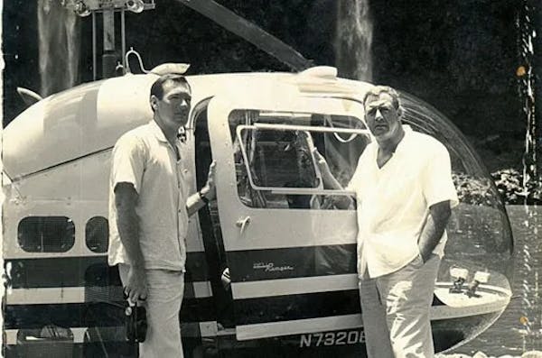 black and white photo of two men next to a helicopter