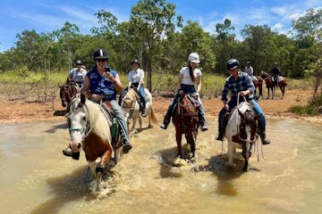 a group of people riding horses through the water
