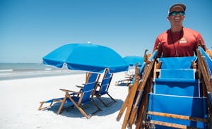 a person sitting in a chair with a blue umbrella on the beach