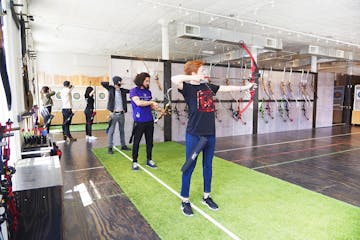 a group of people aiming at an indoor target with a bow and arrow