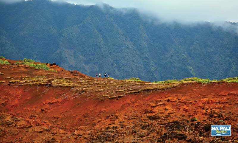Hikers along a red dirt ridge line on the Kalalau Trail Approaching Kalalau Valley