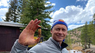 a man smiling for the camera holding up the gold he found while gold panning with country boy mine in breckenridge, colorado