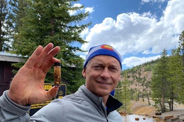 a man smiling for the camera holding up the gold he found while gold panning with country boy mine in breckenridge, colorado