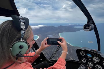 a woman taking pictures aboard a helicopter on custom tour with freycinet air tasmania in freycinet, tasmania