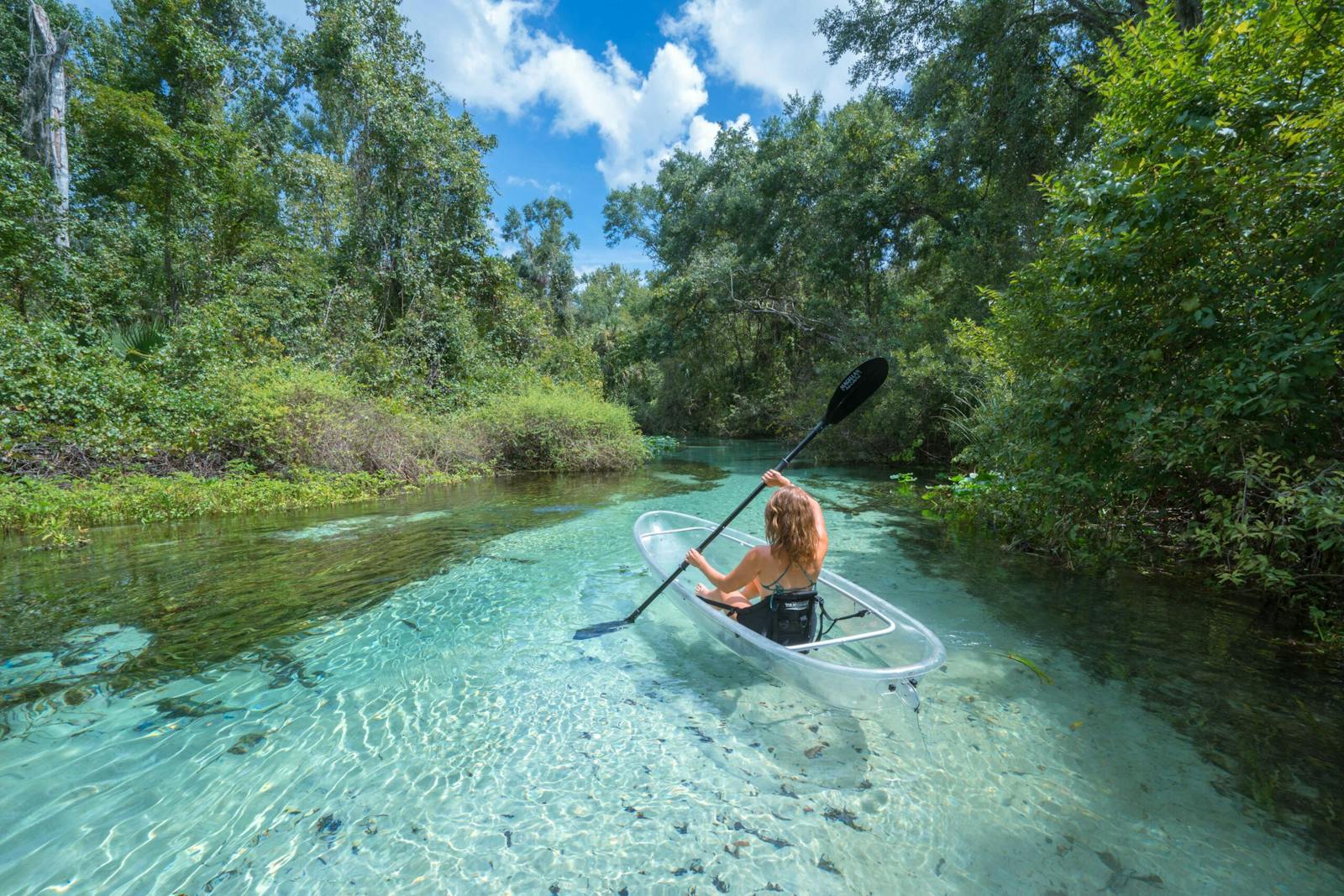 a woman riding on a clear kayak boat in the water