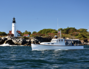 Restored lobster boat the Monhegan passing by Portland Headlight on a sunny day.