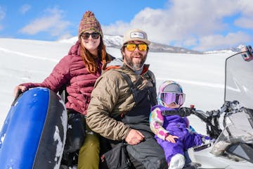 A family of three sitting on a snow tube on a trail at Sage Outdoor Adventures Excursion Resort.