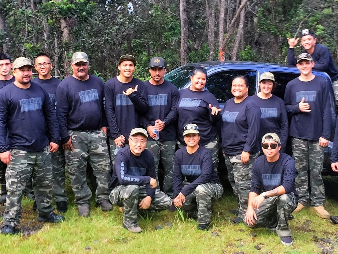 Team auto body with black shirts and camouflage pants in front of a truck in a cloud forest in Hawaii