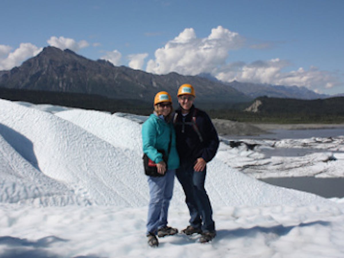 two people smiling in front of mountain on white ice wearing helmets
