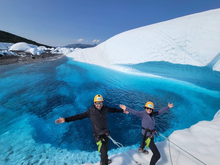 A Man and a Woman tethered in front a blue pool on a glacier